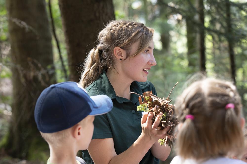 Eine Försterin erklärt Kindern die Wichtigkeit von Laub im Wald.